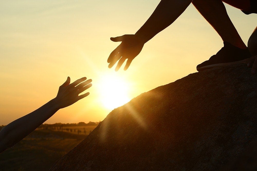 Hiker helping friend outdoors at sunset. Help and support concep