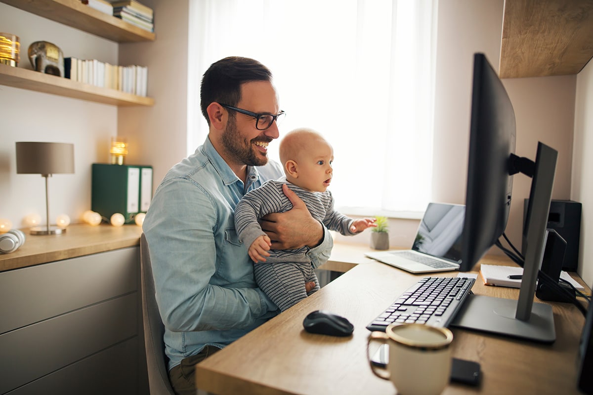 man holding baby while sitting at work desk