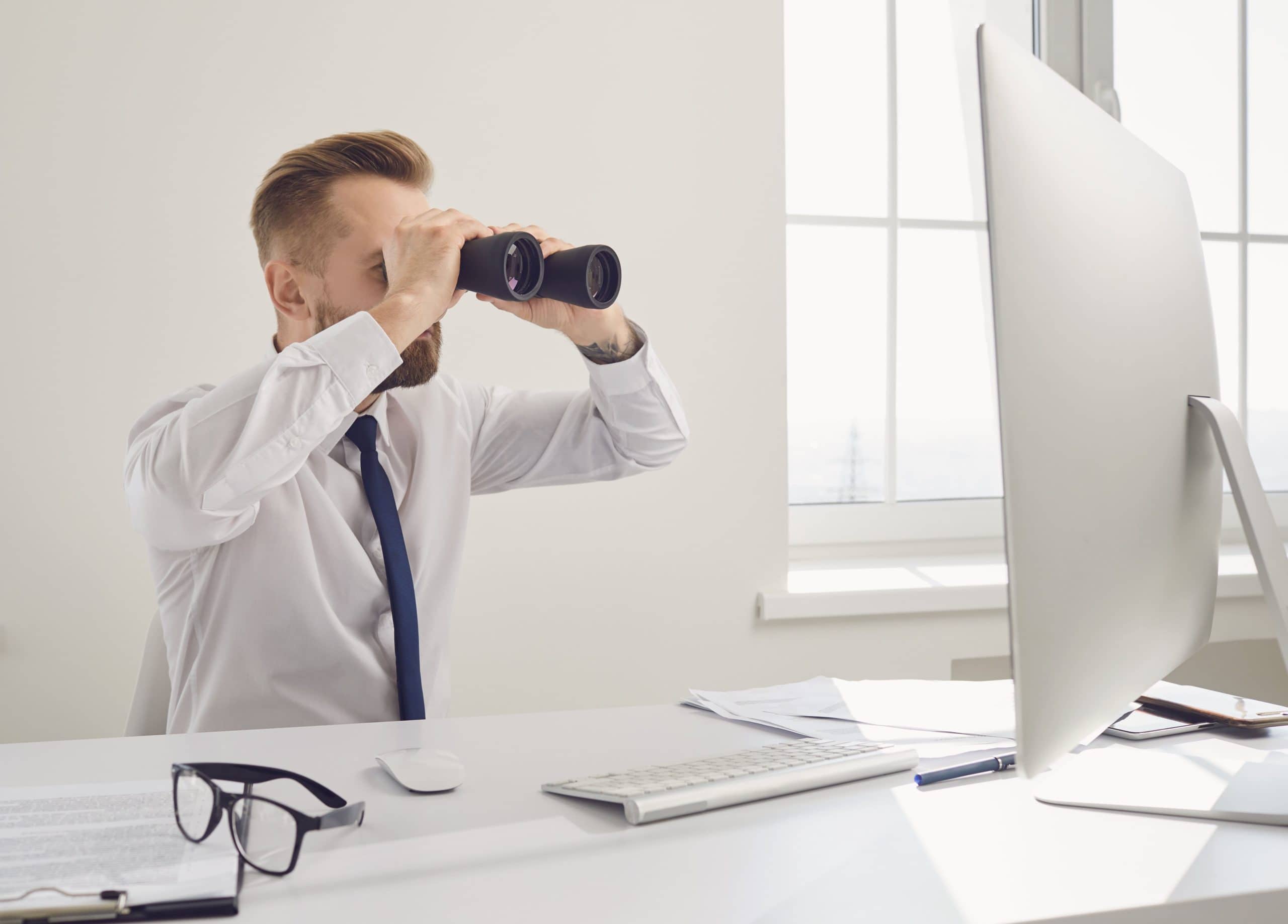 man with binoculars looking at computer screen watching real estate trends
