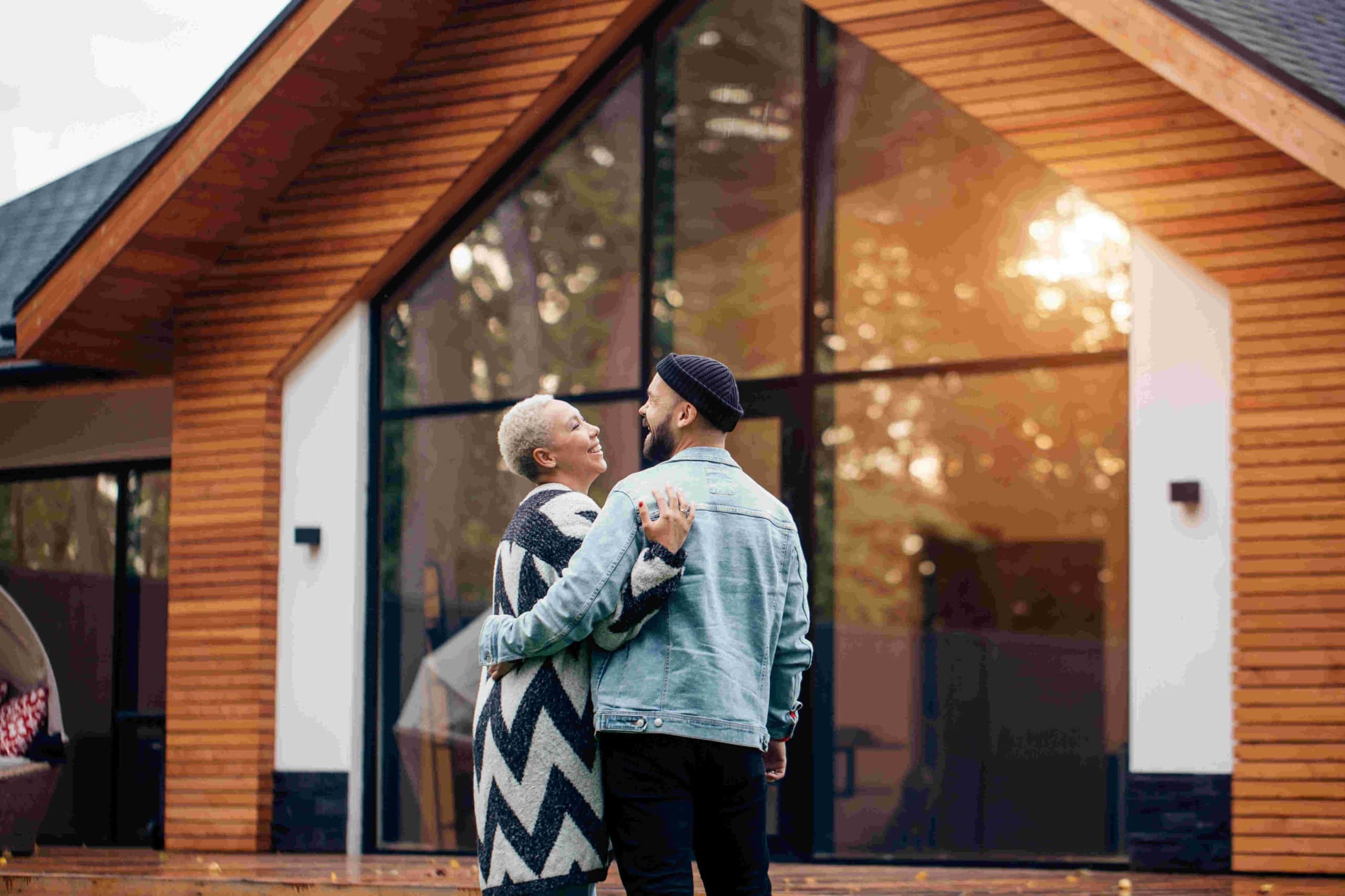 couple smiling in front of large luxury cabin home