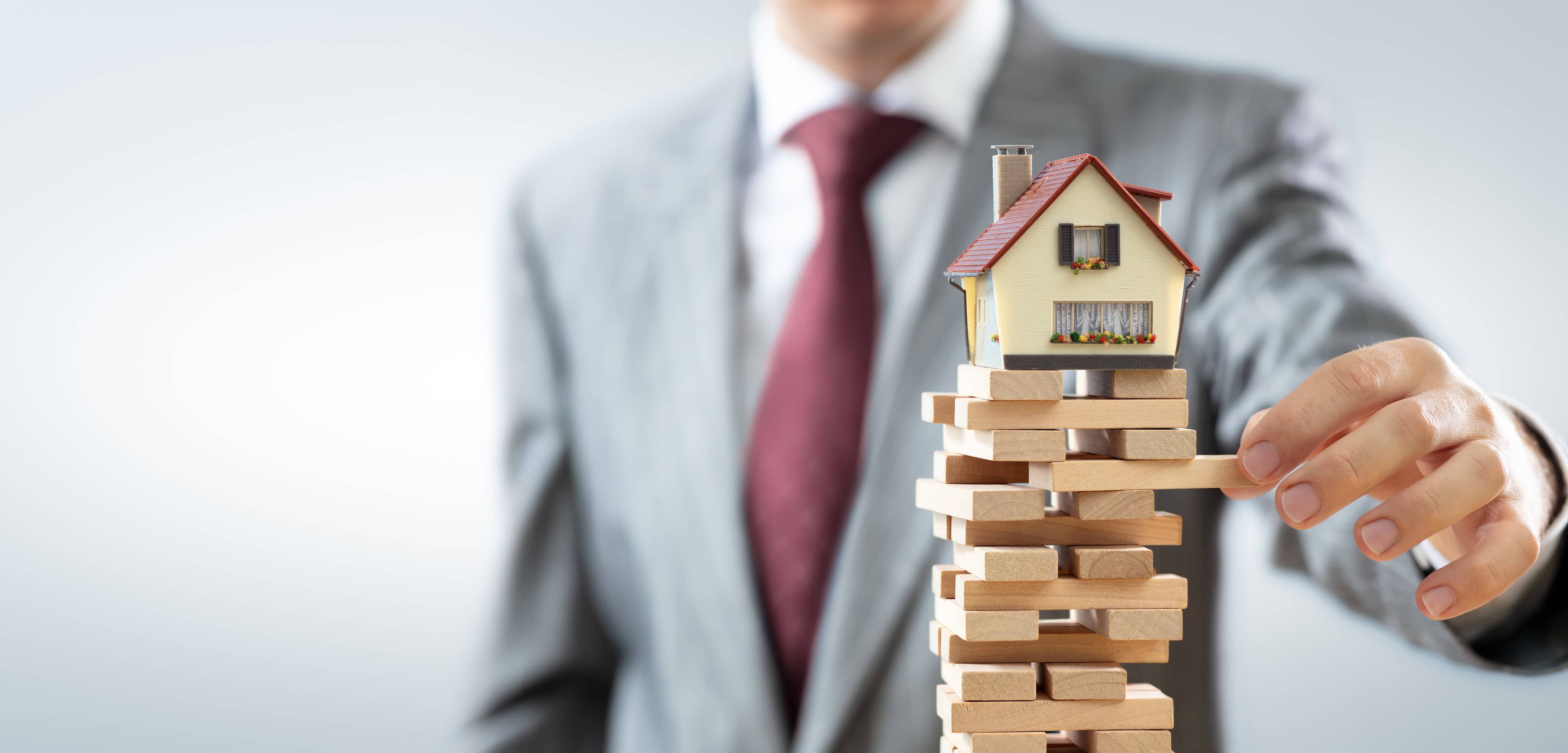 house on top of jenga with man in background real estate market shift