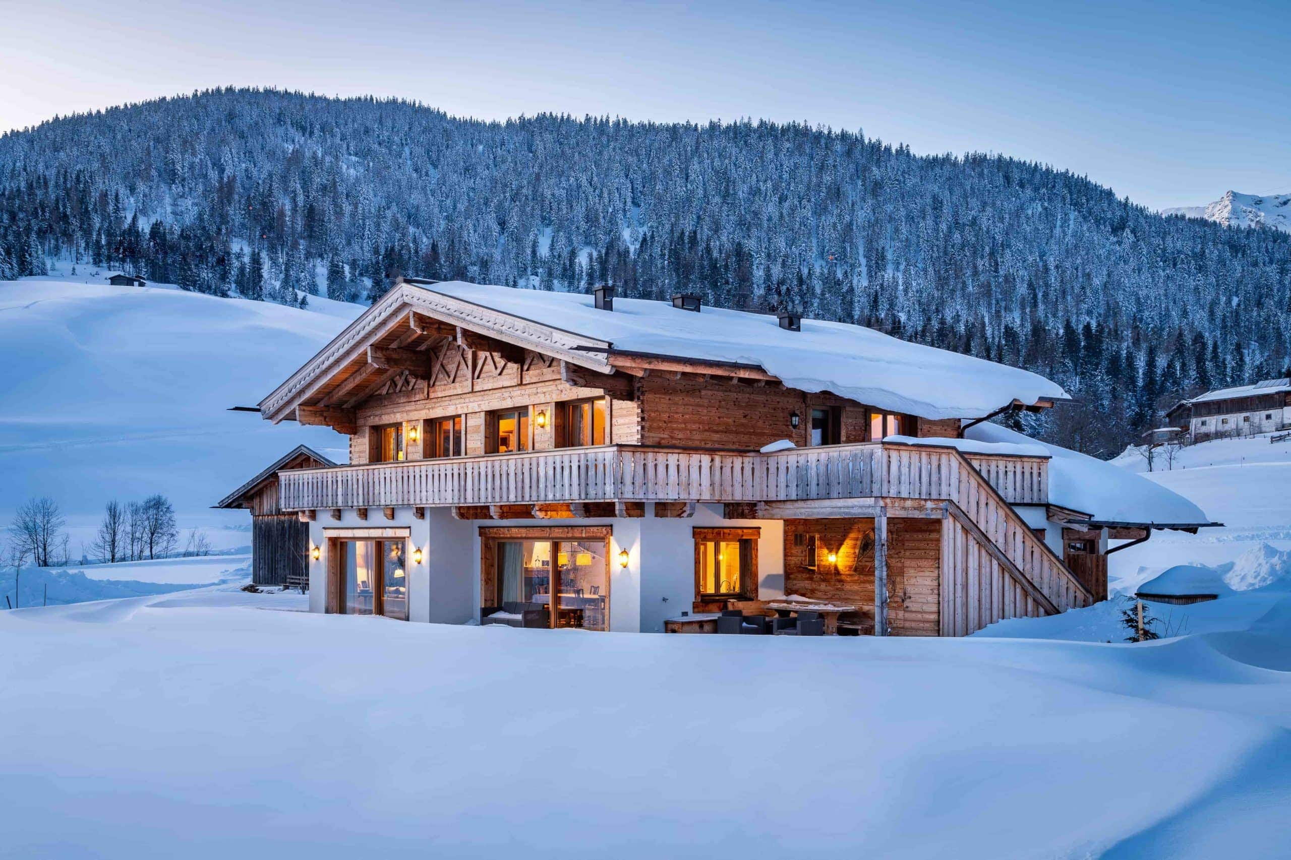 log cabin home covered in snow surrounded by mountains