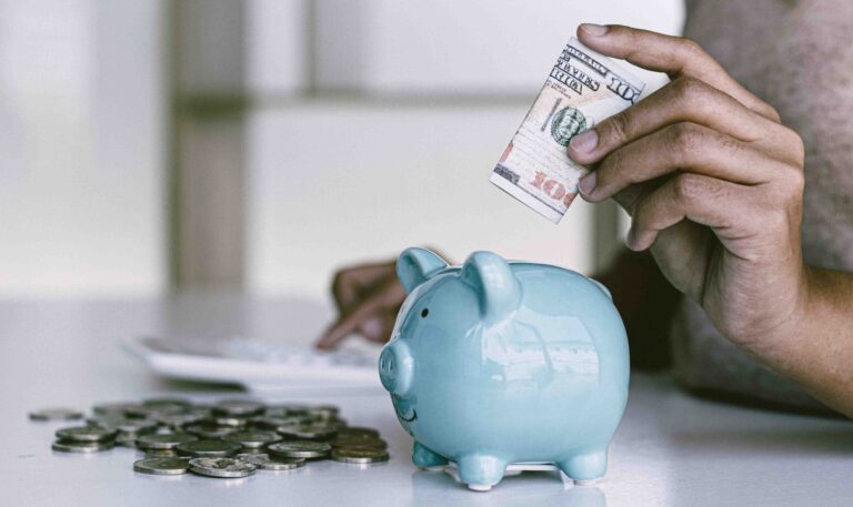 person putting money in blue piggy bank