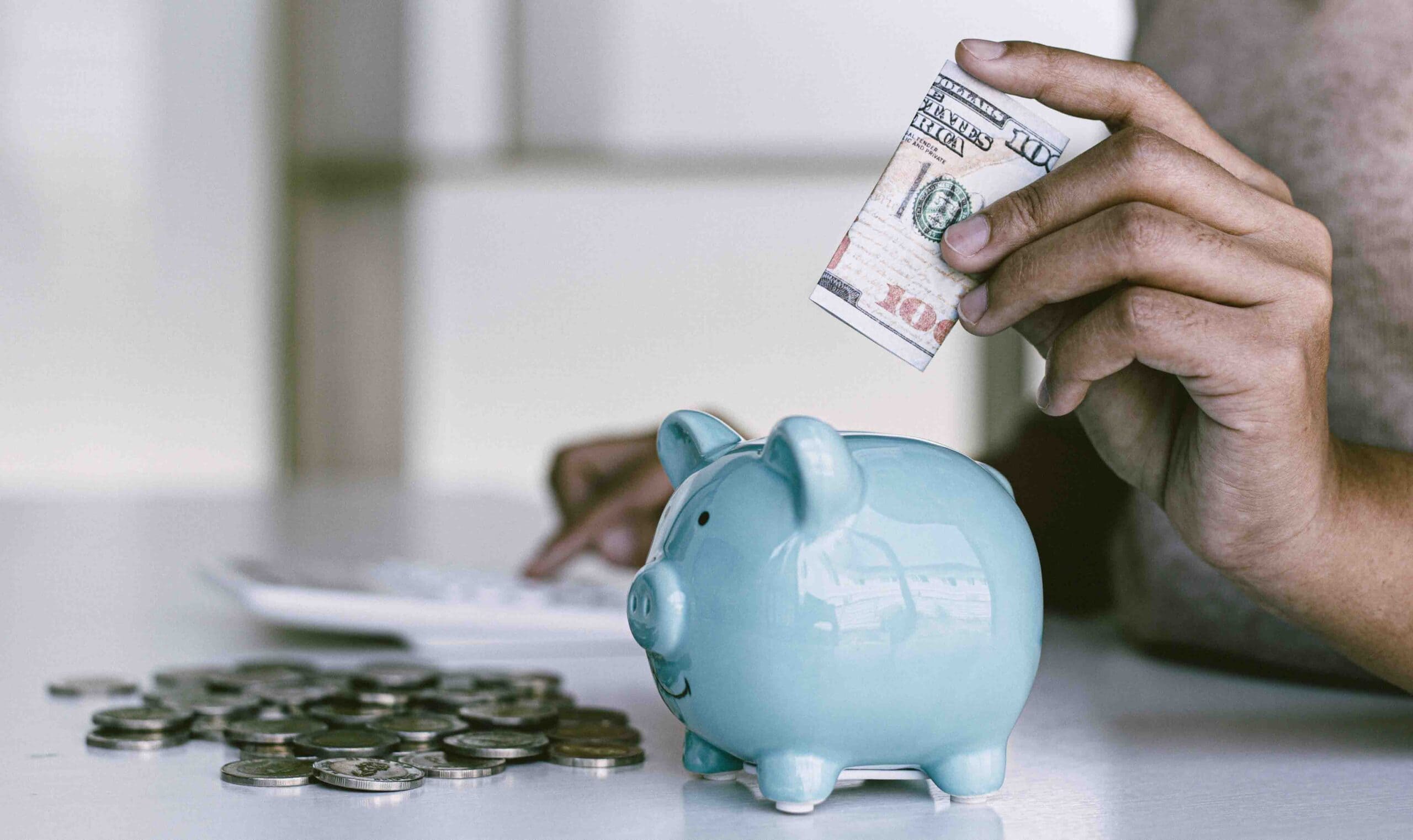 person putting money in blue piggy bank